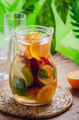 Fototapeta na wymiar Glass jug of white sparkling wine sangria decorated with citrus slices and season fruits on wooden table. 