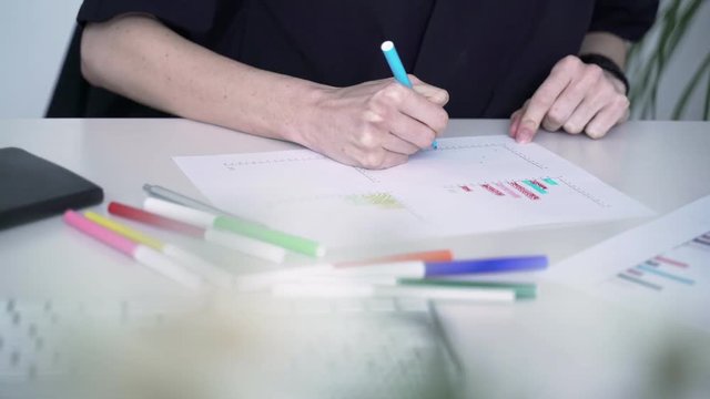 Woman fills data in graphs on paper. Records information. Woman is engaged in office work. Graphic charts,indicators. Woman works at the offside table. Woman draws symbols on the paper