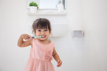 Little cute baby girl cleaning her teeth with toothbrush in the bathroom