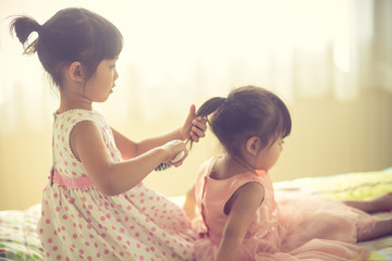 Lovely little girl brushing hair of her sister while sitting on the bed