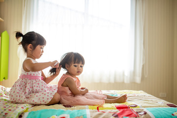 Lovely little girl brushing hair of her sister while sitting on the bed