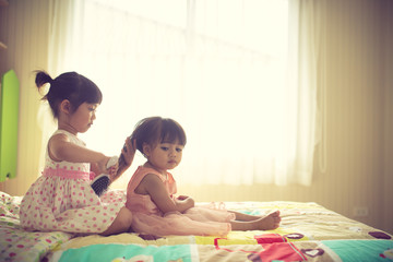 Lovely little girl brushing hair of her sister while sitting on the bed
