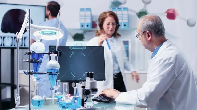 Female and male researcher are talking about a sample from a tube. In the background - modern laboratory with high end equipment