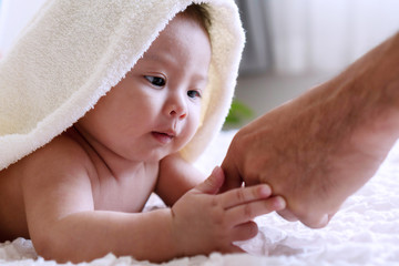 Cheerful cute baby looking at hand his father under white blanket. Innocence baby with parent crawling on white bed with towel on his head at home. Lifestyle relationship concept.