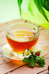 Cup with tea and strawberry on wooden table.