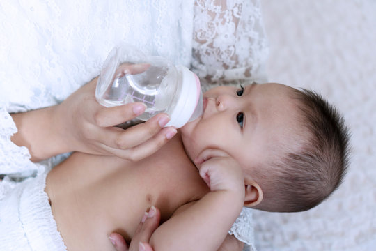 Portrait Cute Baby Boy Drinking Water From Bottle With His Mom. Hand Of Asian Young Woman Holding Bottle With Water While Feeding Aqua For Her Son. Lifestyle Child Concept.