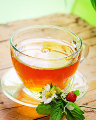 Cup with tea and strawberry on wooden table.