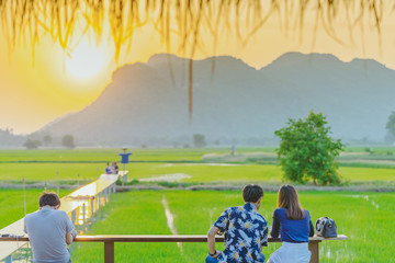 Back view of people sit for resting and waiting for time to take photos of the sunset on the farmer's balcony in the rice fields.