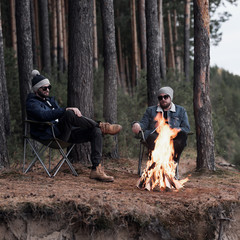 Stylish male friends relaxing by campfire