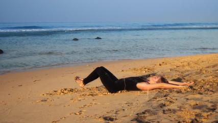 beautiful lady in tracksuit practices yoga exercise Rejuvenation on yellow sand beach near blue boundless ocean extreme slow motion. Concept fitness sport yoga wellness lifestyle