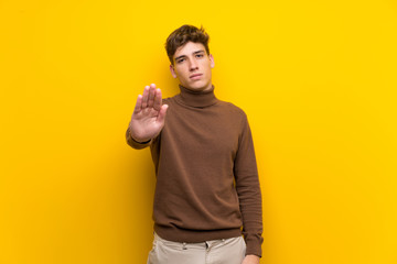Handsome young man over isolated yellow background making stop gesture