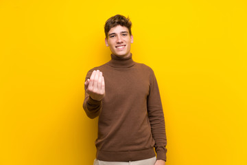 Handsome young man over isolated yellow background inviting to come with hand. Happy that you came