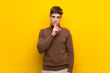 Handsome young man over isolated yellow background showing a sign of silence gesture putting finger in mouth