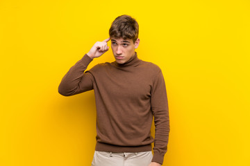 Handsome young man over isolated yellow background making the gesture of madness putting finger on...