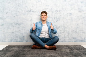 Handsome young man sitting on the floor giving a thumbs up gesture