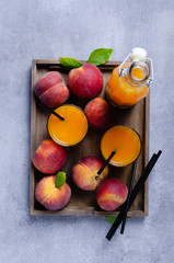 Fresh homemade peach juice in glass for breakfast on wooden tray over grey blue table Rustic stile.