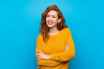Redhead woman with yellow sweater keeping the arms crossed in frontal position