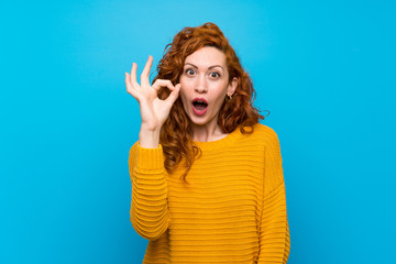Fototapeta premium Redhead woman with yellow sweater surprised and showing ok sign