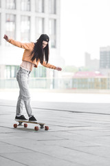 beautiful young woman with outstretched hands riding on skateboard in city