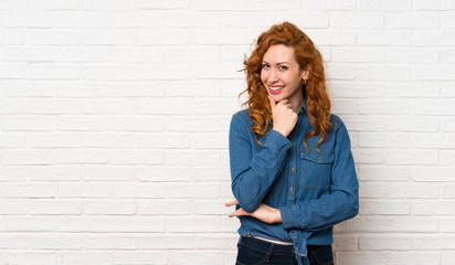 Redhead woman over white brick wall looking to the side