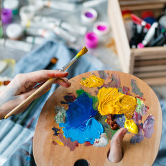 Artist essential tools. Closeup of female hands holding wooden palette and paintbrush over blurred...