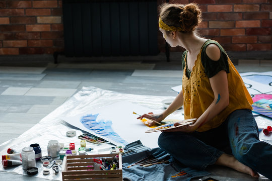 Art hobby and recreation. Female artist sitting on floor, using acrylic paint palette, creating abstract artwork.