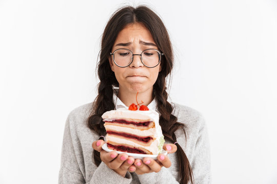Photo closeup of confused teenage girl wearing eyeglasses feeling sad while holding big slice of birthday cake