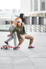 happy man falling from skateboard near young brunette woman