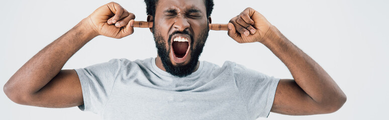emotional african american man in grey t-shirt yelling and closing ears isolated on grey
