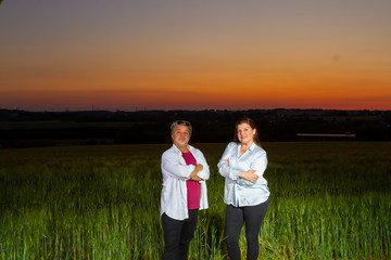 Man and woman poses standing together in an open field at end of the day out in the field with the beautiful landscape that nature presents with the sunset.