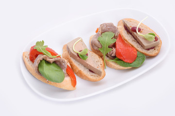 4 small mix sandwiches with pate and meat, grilled paprika. on a white oval plate. isolated on white background
