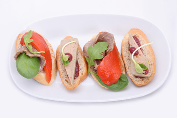 4 small mix sandwiches with pate and meat, grilled paprika. on a white oval plate. isolated on white background