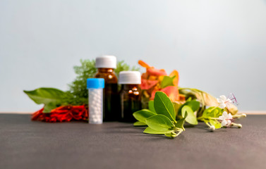 Obraz na płótnie Canvas Homeopathic Concept - Blurred image of homeopathic medicine bottles with white,red,orange flowers and green leaves