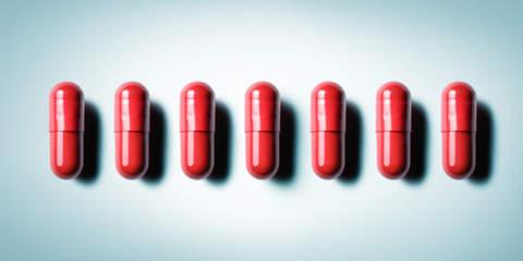 Row of red capsules on blue grey background. Conceptual image for healthcare and pharmaceutical industry,
