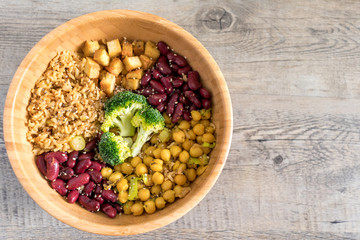 Vegan buddha bowl with stir fry tofu, brown rice, broccoli, red kidney beans, cooked chickpeas, seeds and vegetables. Flat lay on wooden surface with copy space.