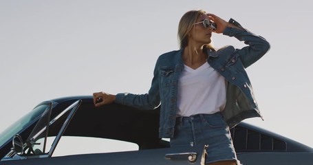 Attractive model woman in denim jacket flipping her hair and leaning on classic vintage sports car - Powered by Adobe