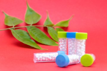Homeopathy Concept - Homeopathic lactose sugar globules in bottles on pink background with green leaf