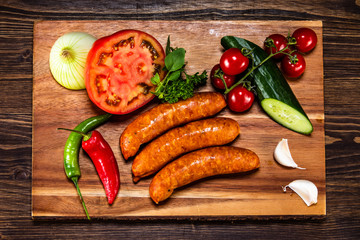 Raw sausages and vegetables on cutting board