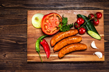 Raw sausages and vegetables on cutting board
