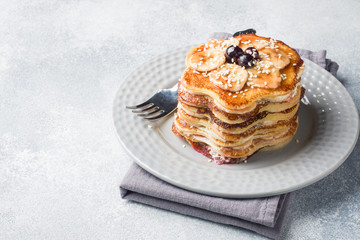 Pancake cake with bananas and berry syrup, selective focus, grey background.