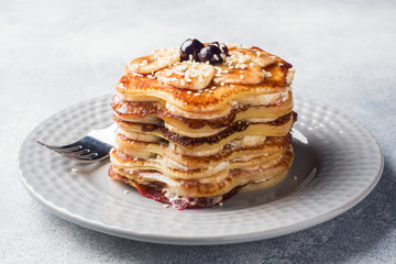 Pancake cake with bananas and berry syrup, selective focus, grey background.