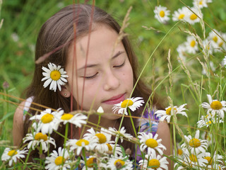 Portrait of a smiling teenager girl among meadow flowers. Happy child in nature.