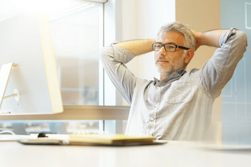 Obraz premium Relaxed businessman sitting at desk with arms behind head