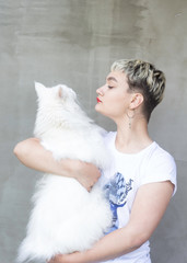 Young attractive fashion girl hugging a white maine coon cat in her arms. The girl the blonde in a white t-shirt with a cat's portret.