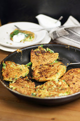 Proper nutrition, vegetarian breakfast gluten free,zucchini courgette pancakes with beans, mint on frying pan with sour greek yogurt, black background, towel, fork, knife on wooden surface