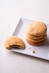 Homemade stack of shortbread chocolate cookies with one bitten cookie on white plate wooden table