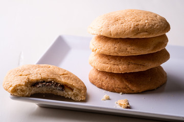 Homemade stack of shortbread chocolate cookies with one bitten cookie on white plate wooden table