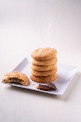 Homemade stack of shortbread chocolate cookies with one bitten cookie and two pieces of chocolate on white plate wooden table