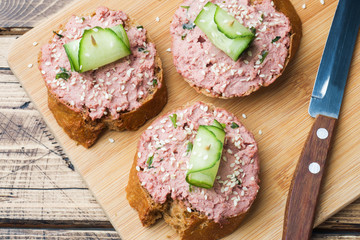 Sandwiches with chicken pate and cucumber on wooden table.