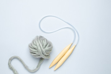 Circular knitting needles and thick grey yarn on blue background